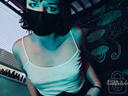 Ryder looking downwards toward cam in blue light. They wear a white slip dress and medical mask